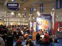Large room with many people playing games at tables under Kosmos signs